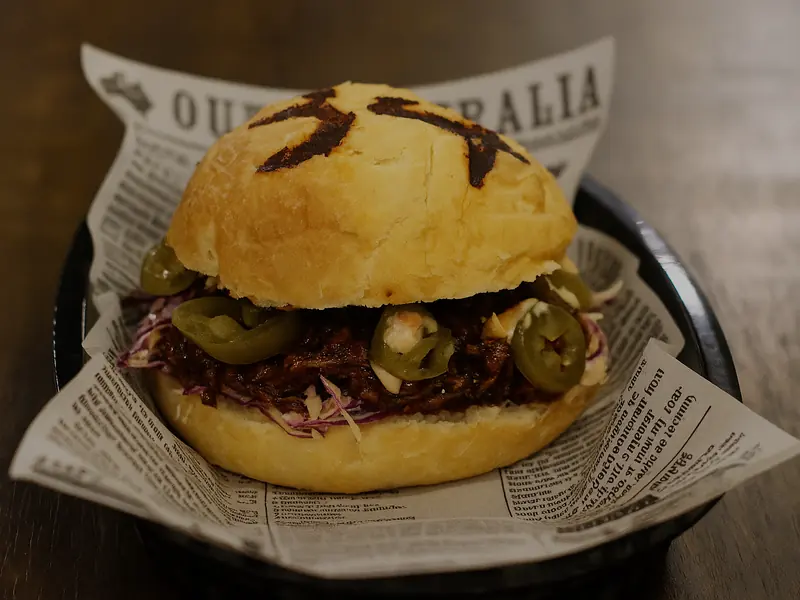 A burger filled with pulled beef, slaw and sliced jalapenos in a golden bun, sitting on newsprint paper.